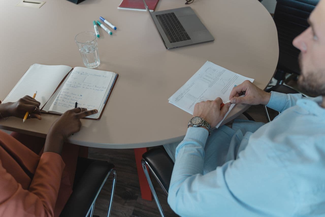 Deux personnes autour d'une table, carnet ouvert et documents annotés — un audit technique commence par une conversation, pas par un accès au code.