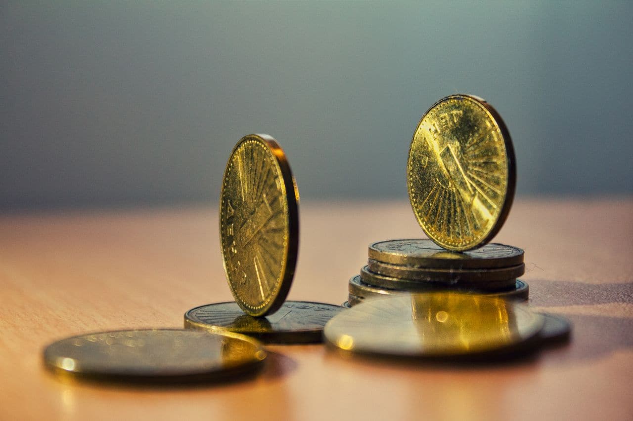 Pièces de monnaie empilées et éparpillées sur une table — les intérêts d'une dette, qui s'accumulent chaque mois sans figurer sur aucune ligne du budget.