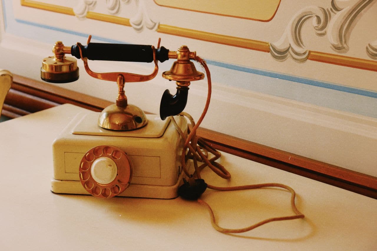 Téléphone vintage à cadran posé sur un guéridon dans une salle de réception — l'objet qui recueille les messages des invités, et qu'il faut expédier, suivre et récupérer.
