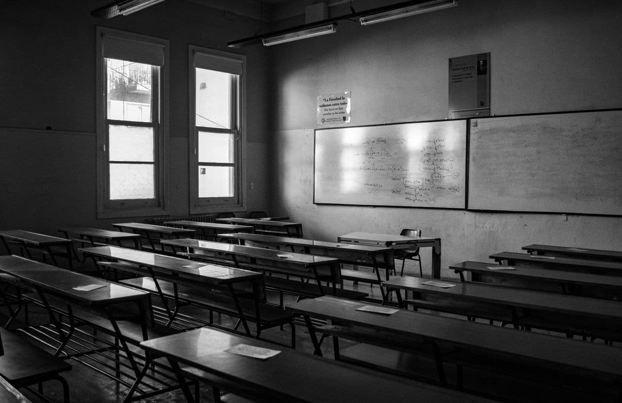 Salle de cours désertée en noir et blanc, tableau encore couvert d'équations et feuilles laissées sur les pupitres — ce qu'il reste d'une formation trois semaines plus tard.
