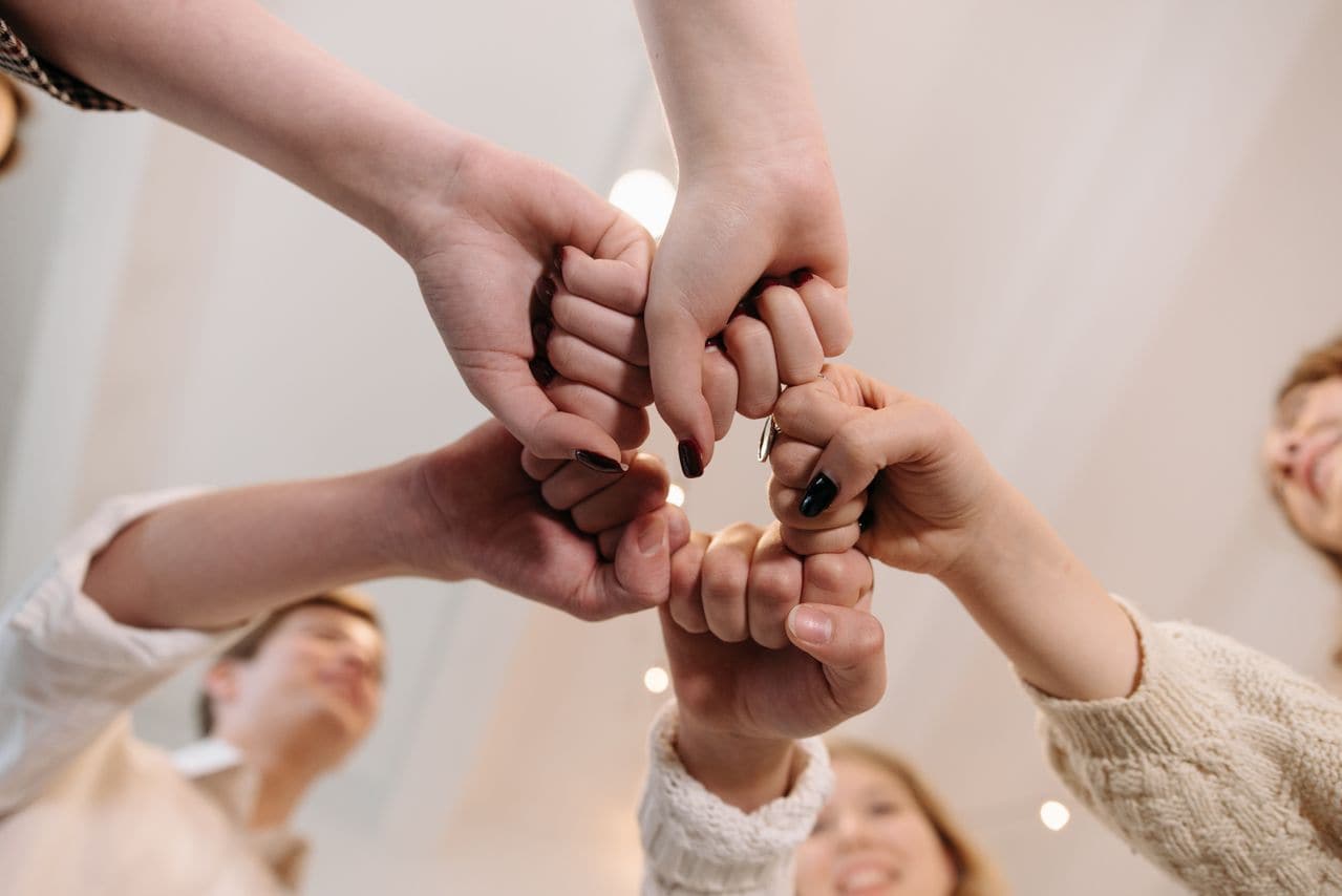 Plusieurs bénévoles réunissent leurs poings en cercle — un collectif, et tout le risque que le numérique de l'association ne repose en réalité que sur une seule de ces mains.