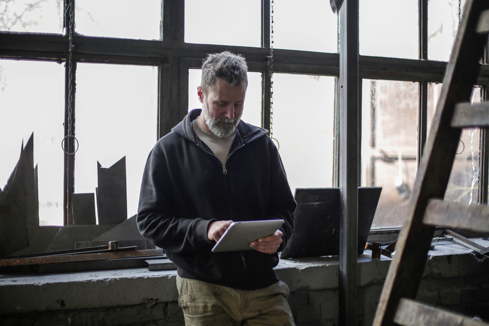 Un artisan consulte une tablette dans son atelier, devant une grande verrière.