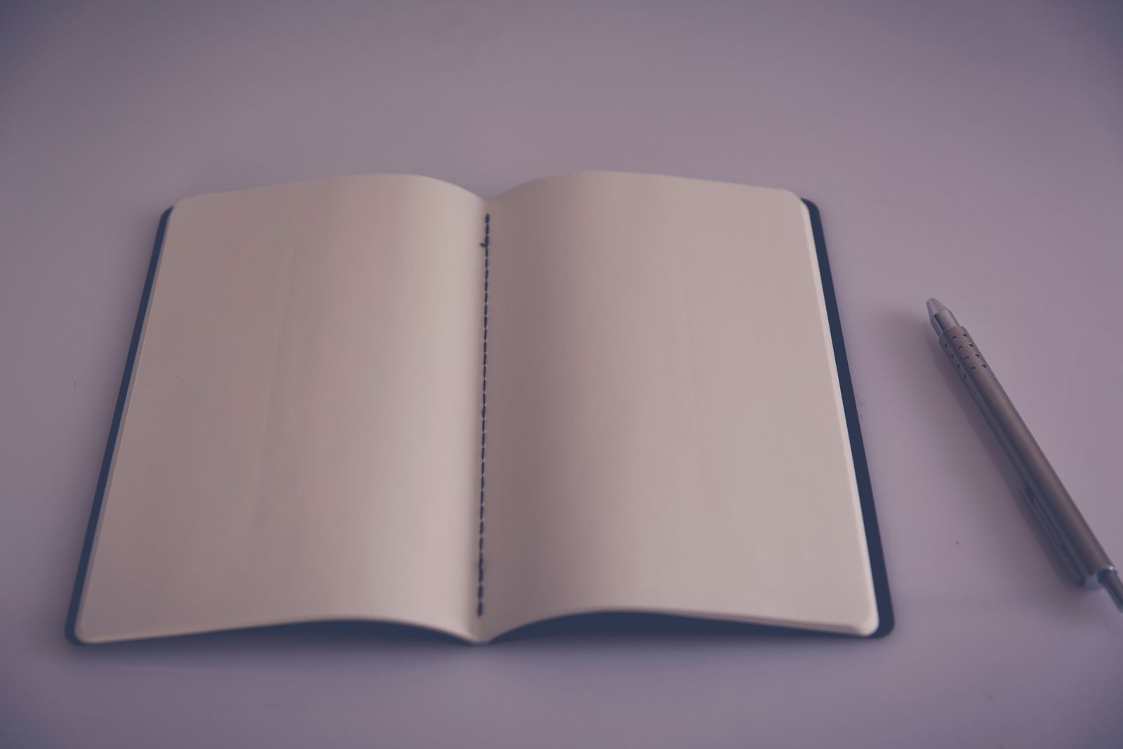 Carnet ouvert sur une page blanche, stylo posé en travers, sur une table claire.