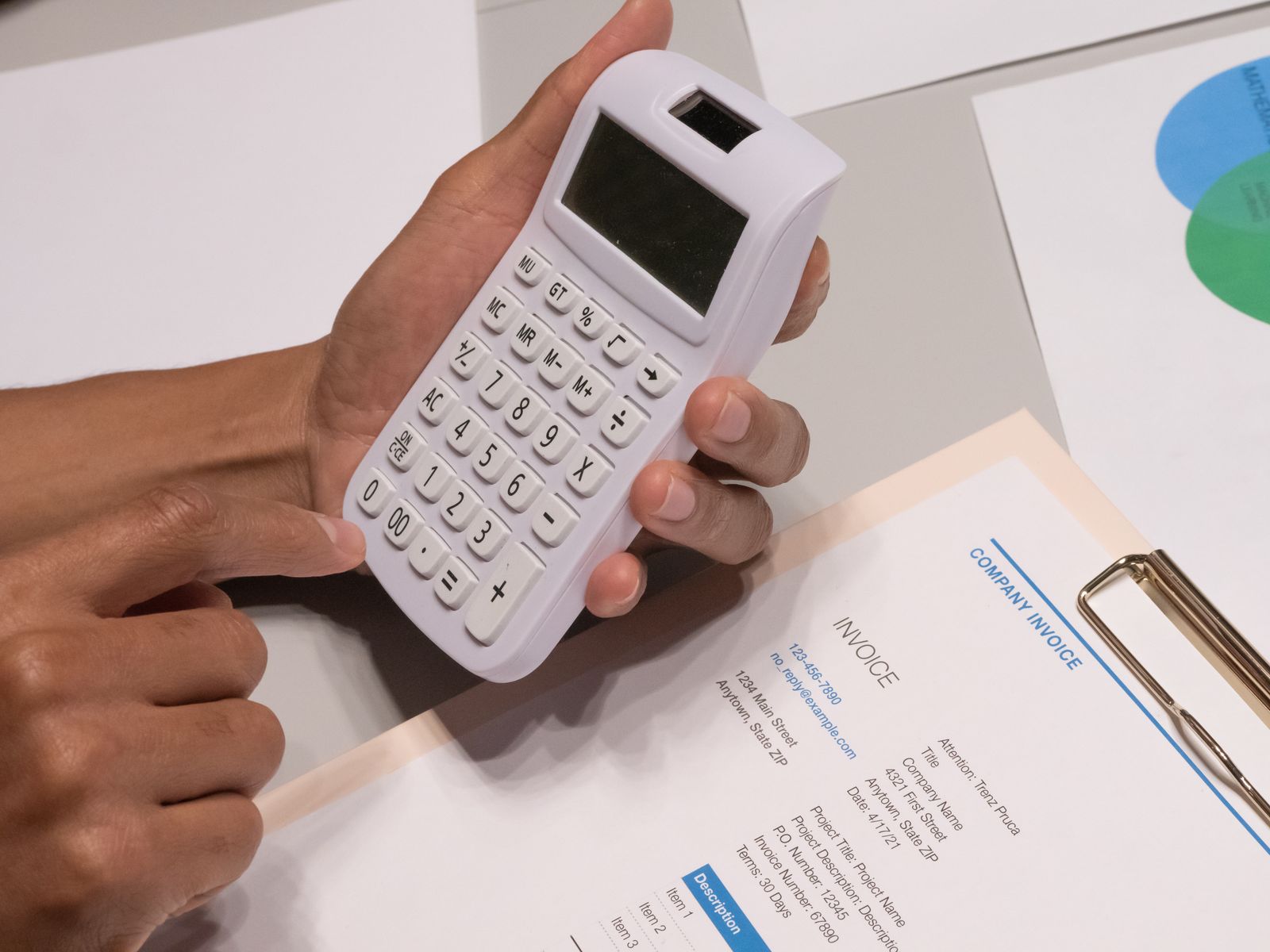 Mains pianotant sur une calculatrice, à côté d'une facture d'entreprise imprimée.
