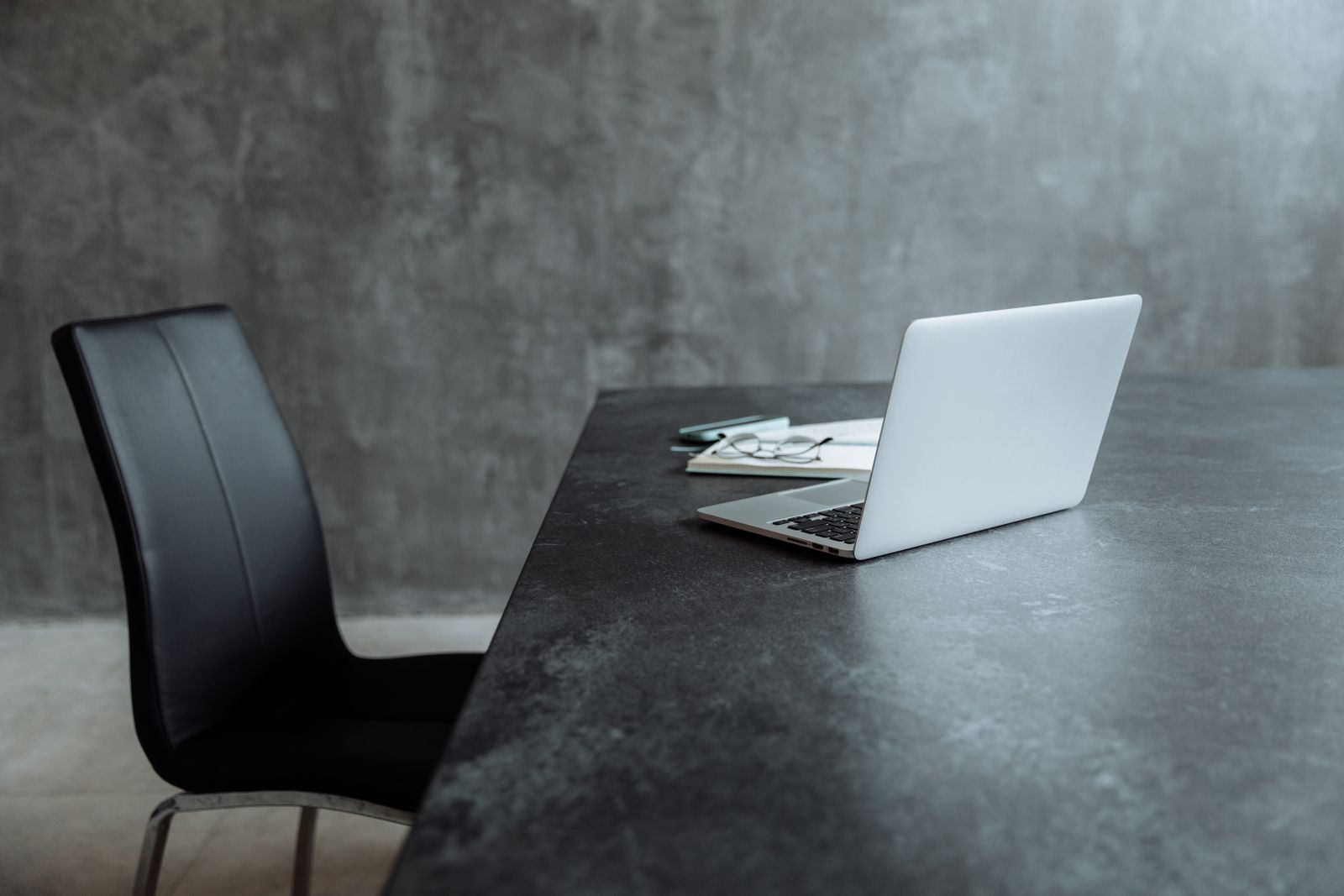 Ordinateur portable posé sur une table sombre, face à un fauteuil vide, dans un bureau épuré.