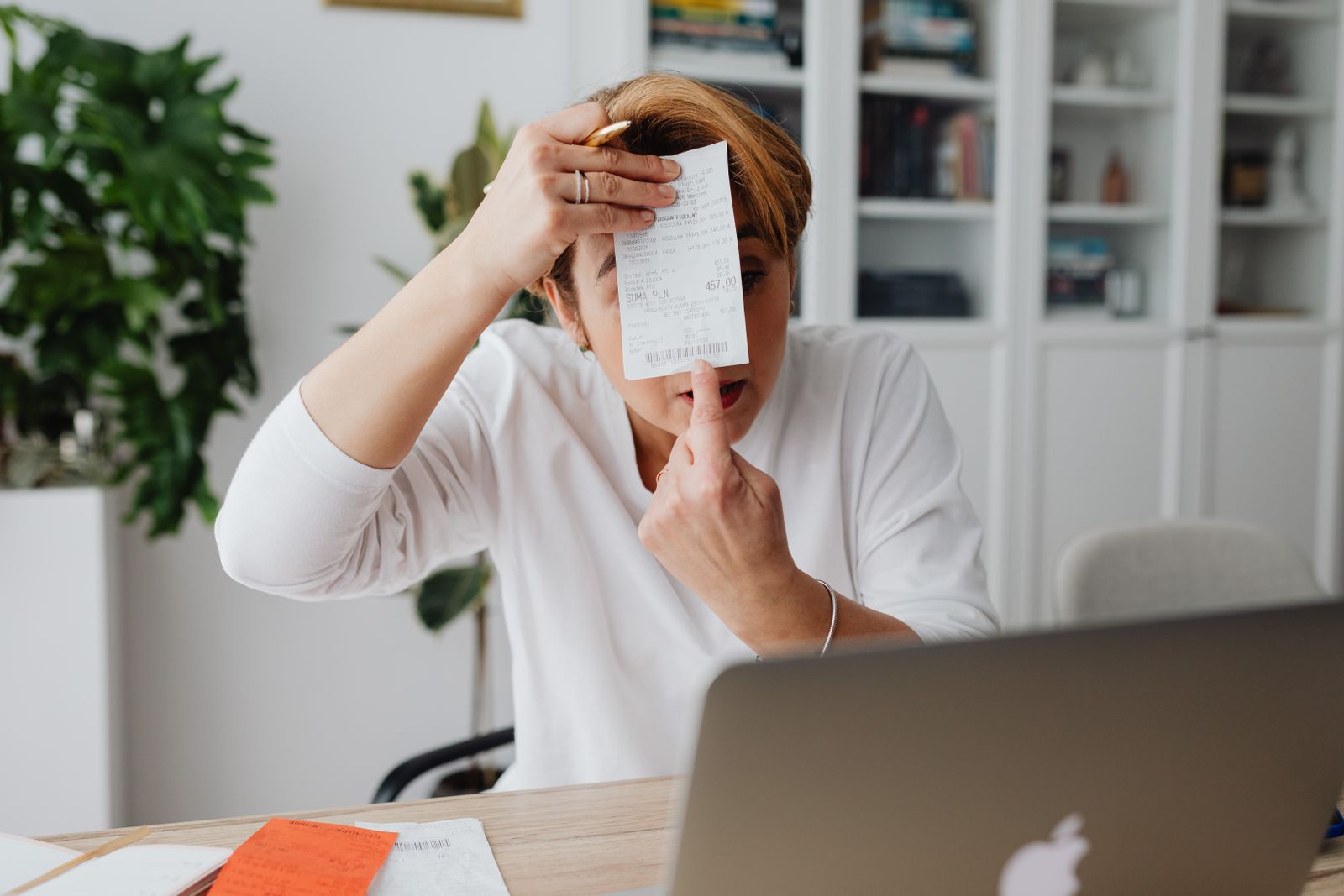 Personne assise à un bureau, tenant un justificatif imprimé devant un ordinateur portable.