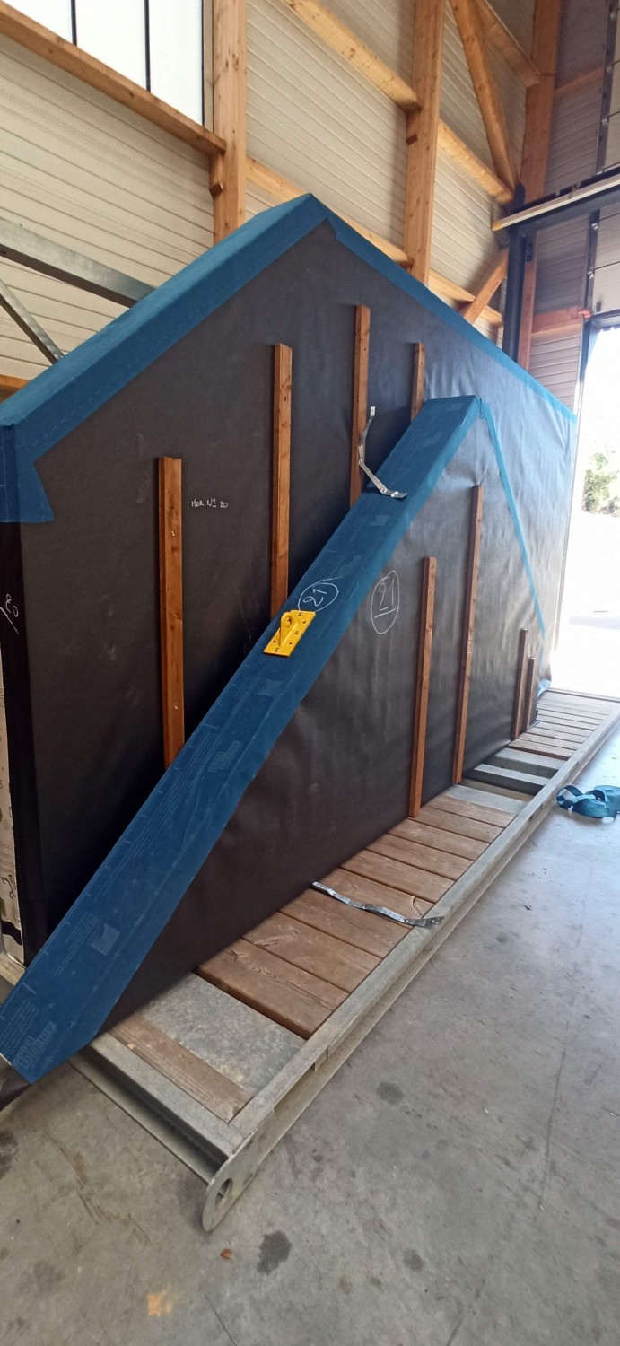 Deux éléments d'ossature bois protégés par un pare-pluie, stockés sur un rack dans l'atelier de MCA SCOP.