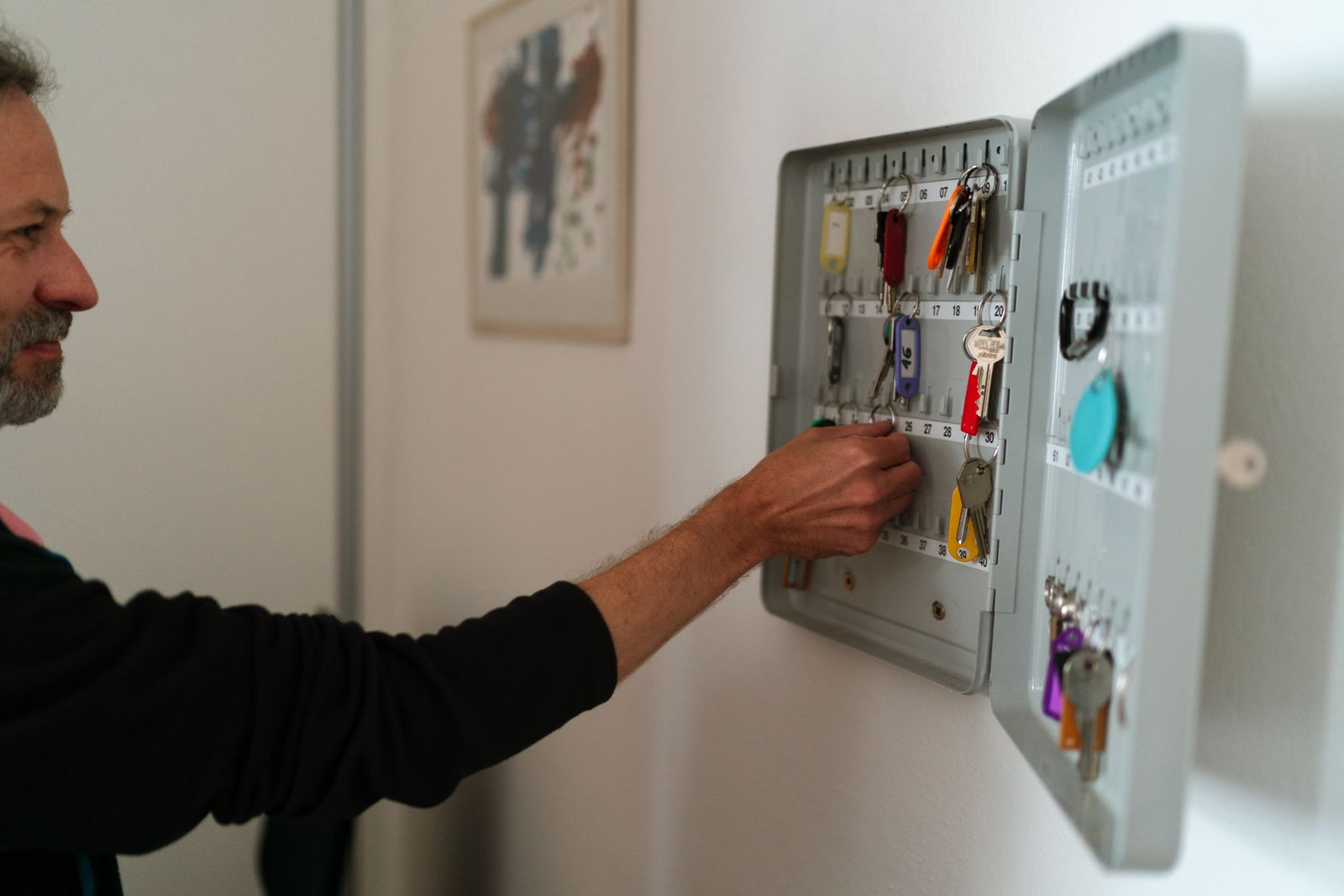 Une personne range des clés étiquetées dans une armoire à clés murale, dans un bureau.
