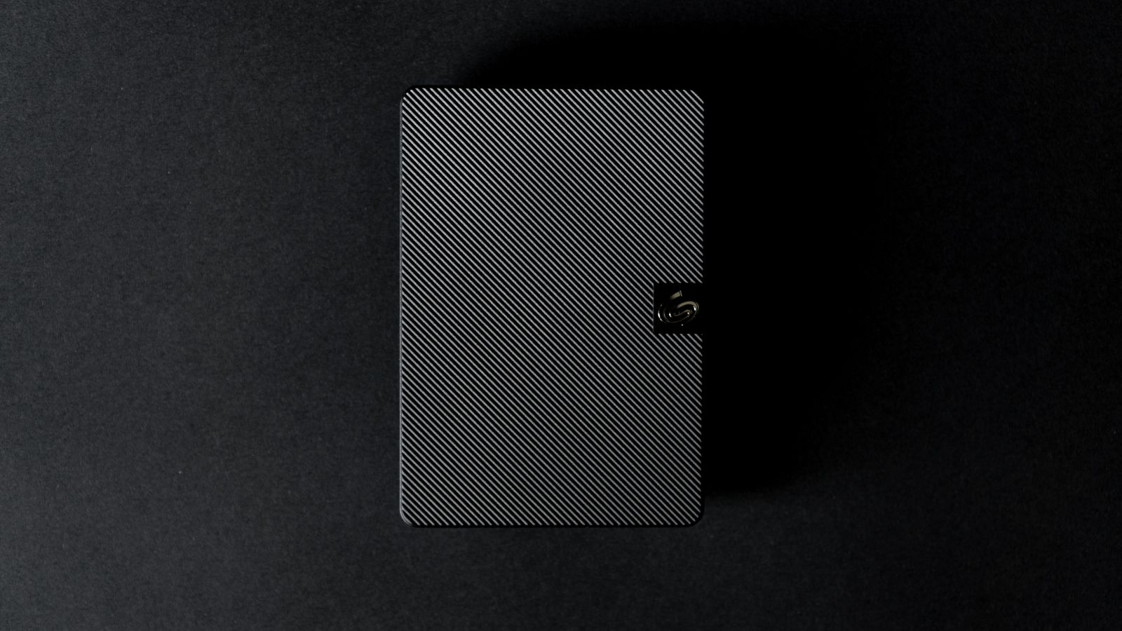 Disque dur externe posé sur fond noir, éclairé de biais.