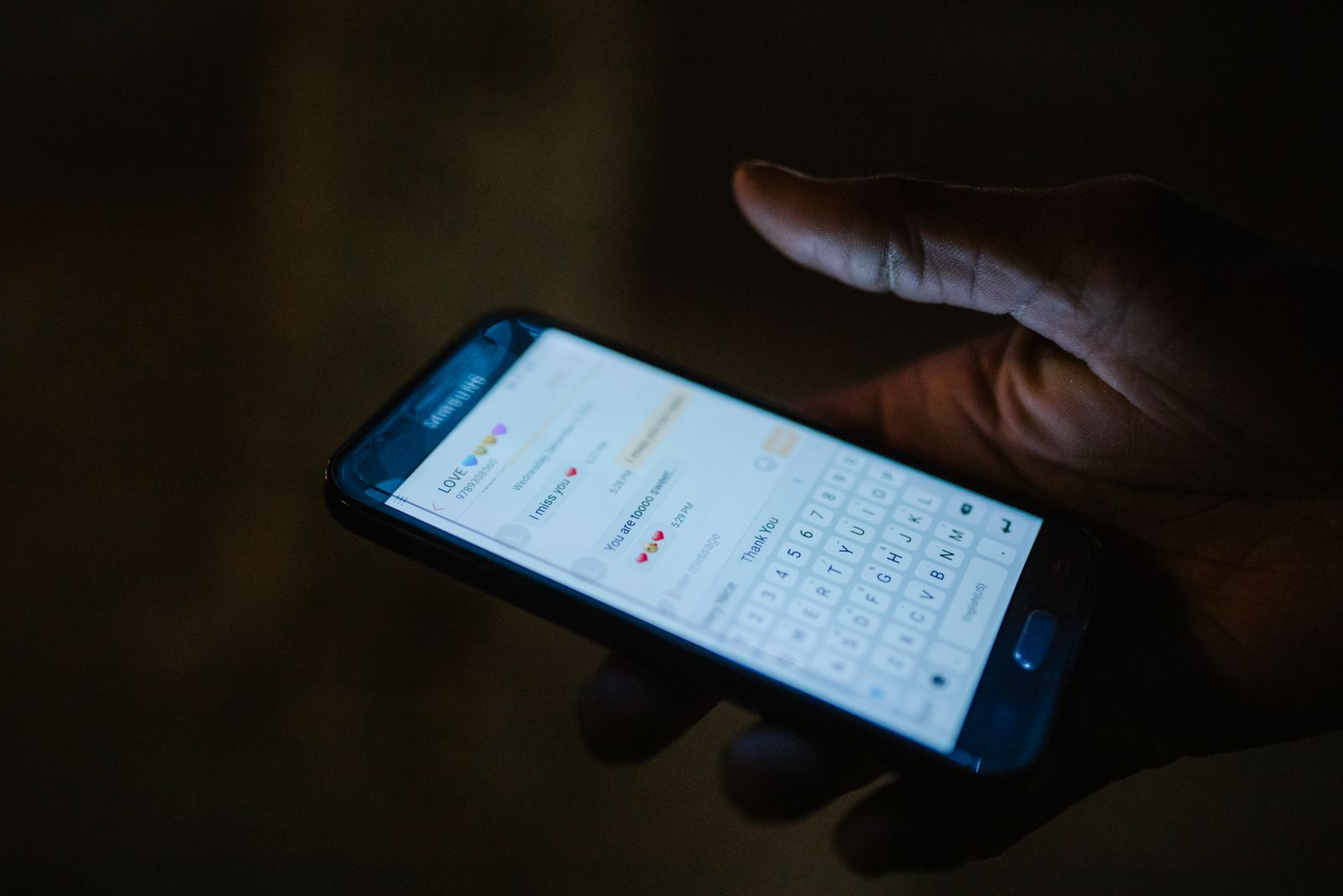 Main tenant un smartphone dont l'écran éclaire une conversation en cours, dans la pénombre.