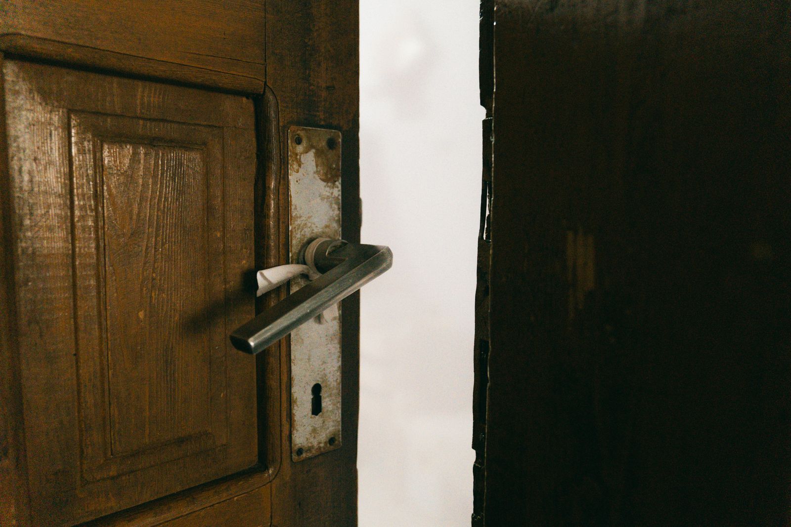 Porte en bois entrouverte sur un intérieur sombre, poignée métallique au premier plan.